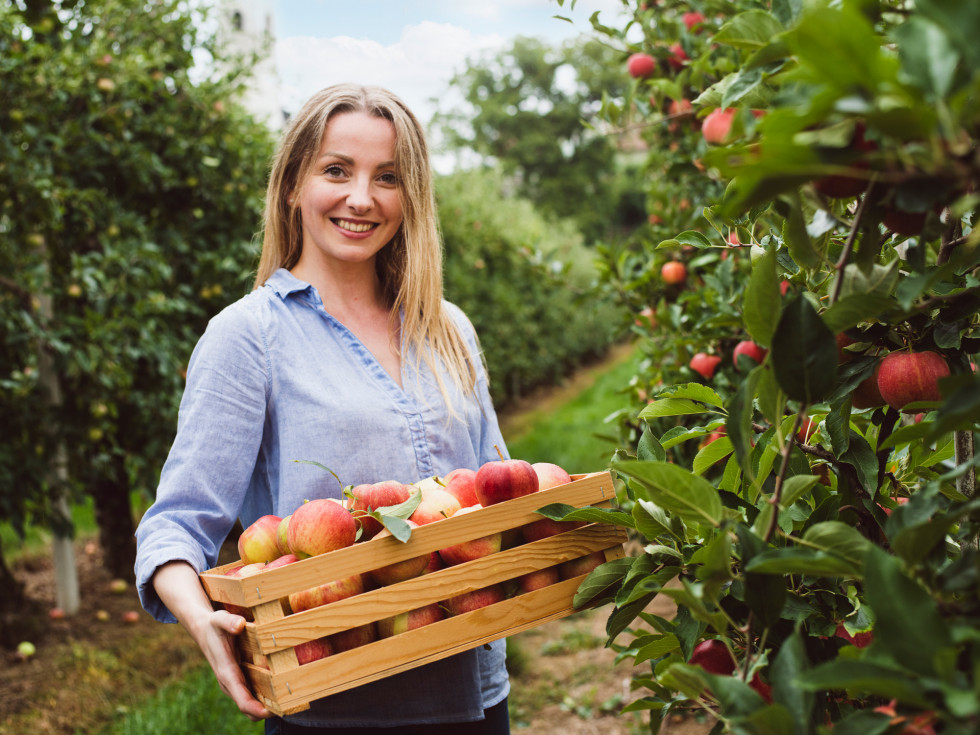 Mlada ženska z zabojem jabolk v sadovnjaku