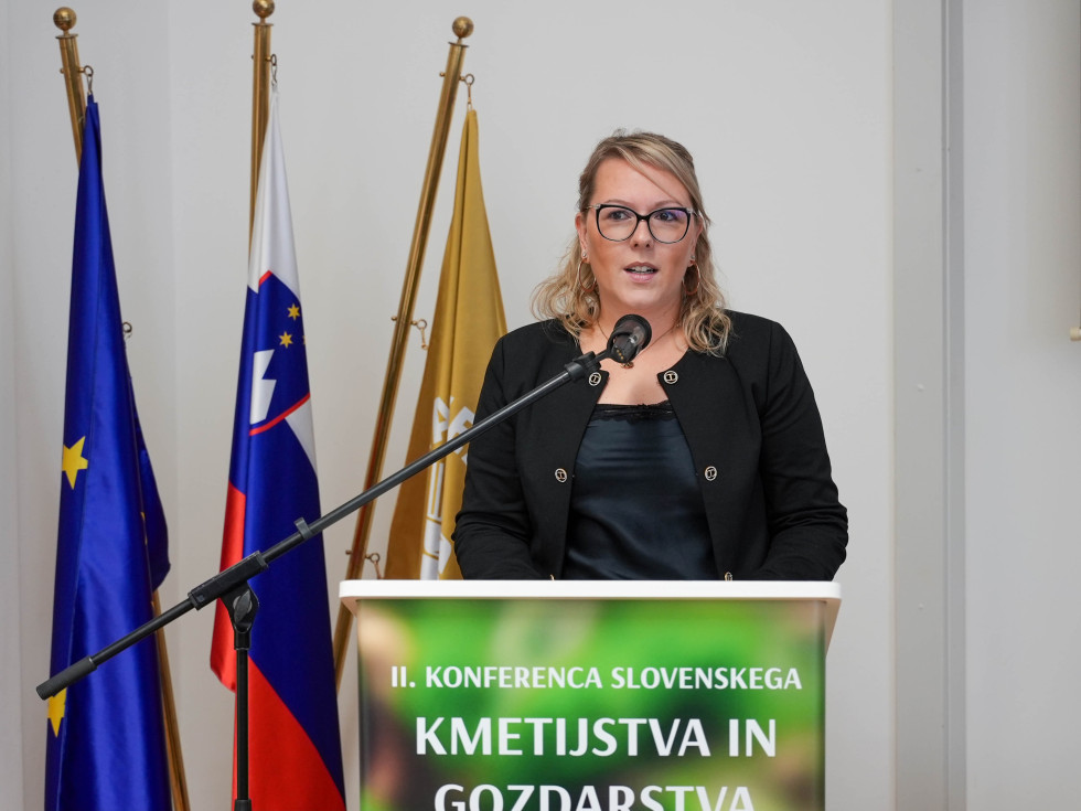 Ministrica stoji za govorniškim pultom in govori.