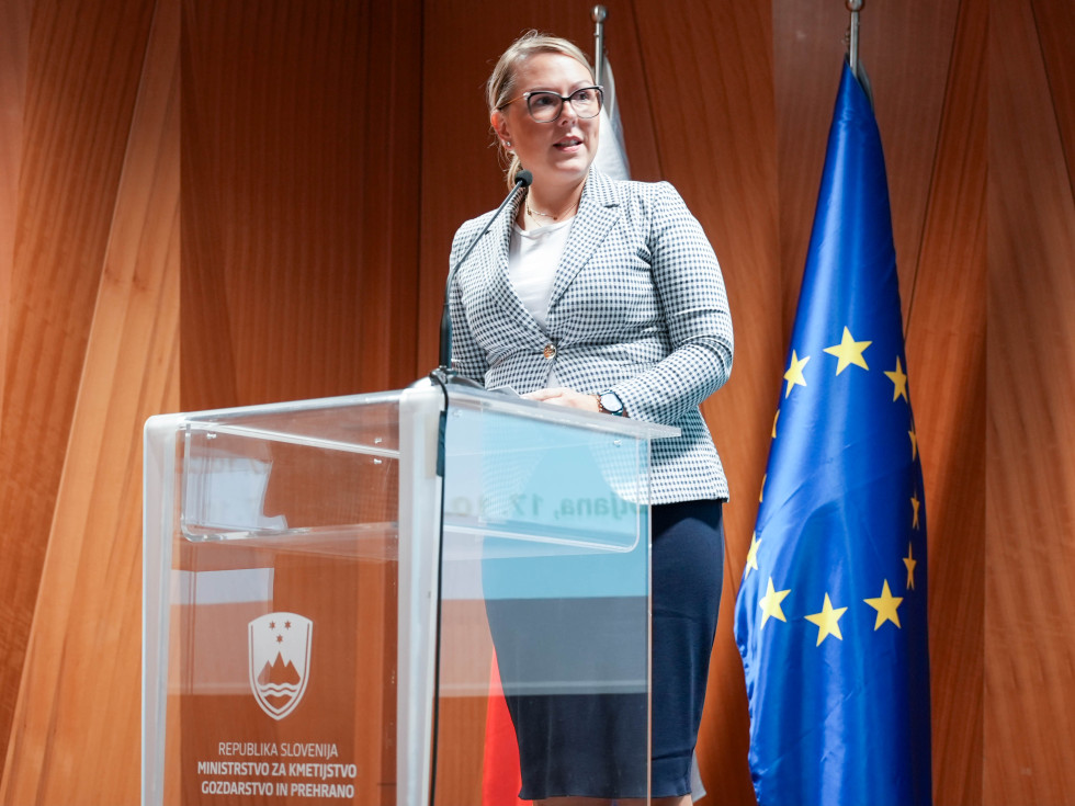 Ministrica stoji za govorniškim pultom in govori.