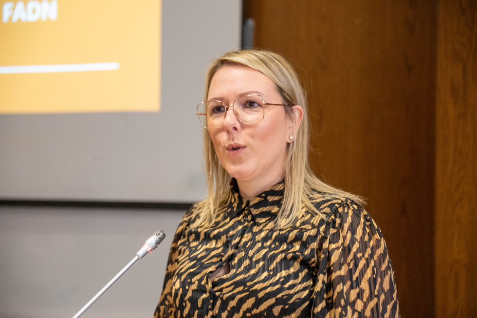 Ministrica stoji za govorniškim pultom in govori.