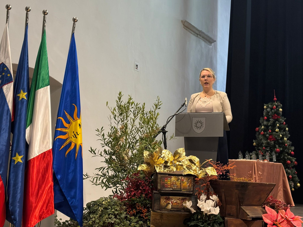 Ministrica stoji za govorniškim pultom in govori.