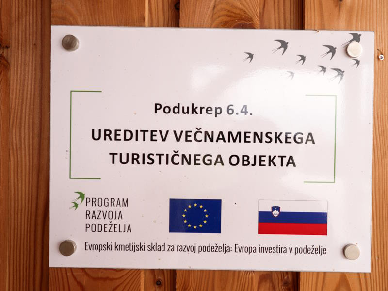 Fotografija obešenega obvestila na leseni steni. Napis: Podukrep 6.4., ureditev večnamenskega turističnega objekta. 