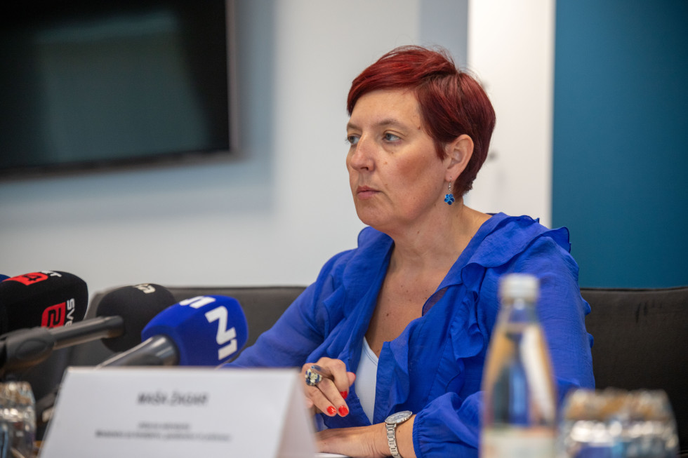 Državna sekretarka sedi na stolu in govori.