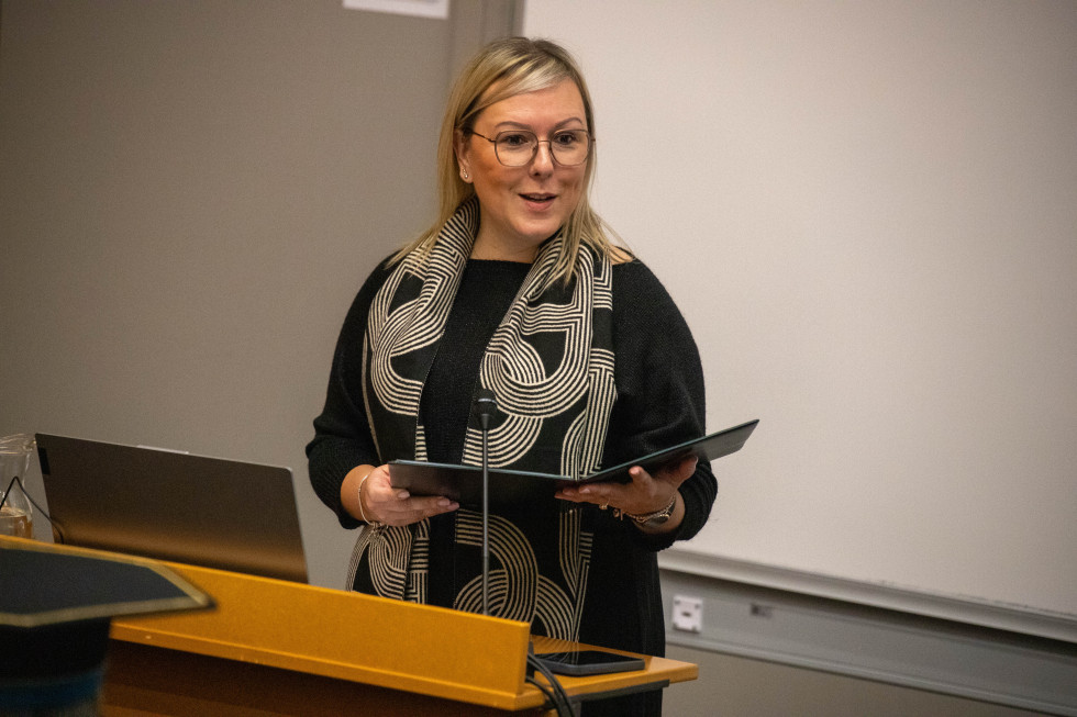 Ministrica stoji za govorniškim pultom in govori. 