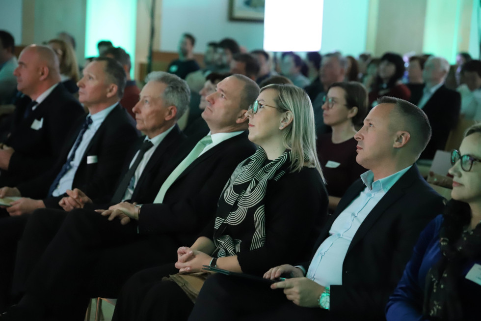 Več oseb sedi na stolih in poslušajo prireditev. 