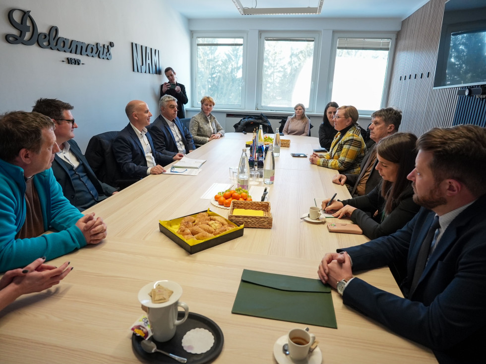 Za mizo na levi in desni strani sedijo ljudje, v ozadju okno