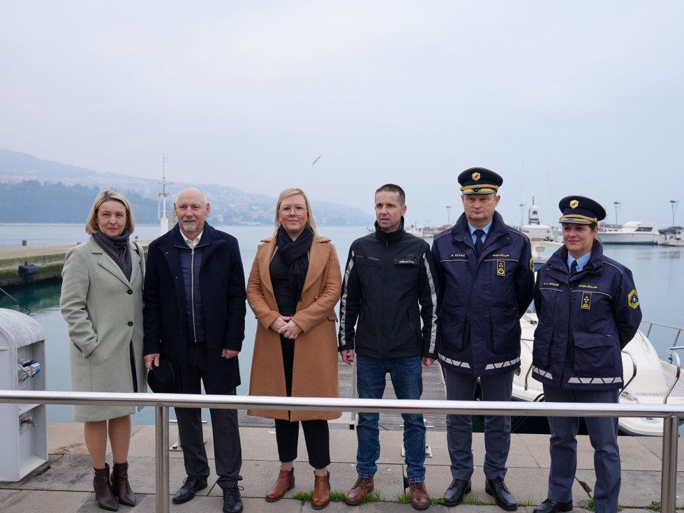 Več oseb stoji na pomolu in se fotografira. 