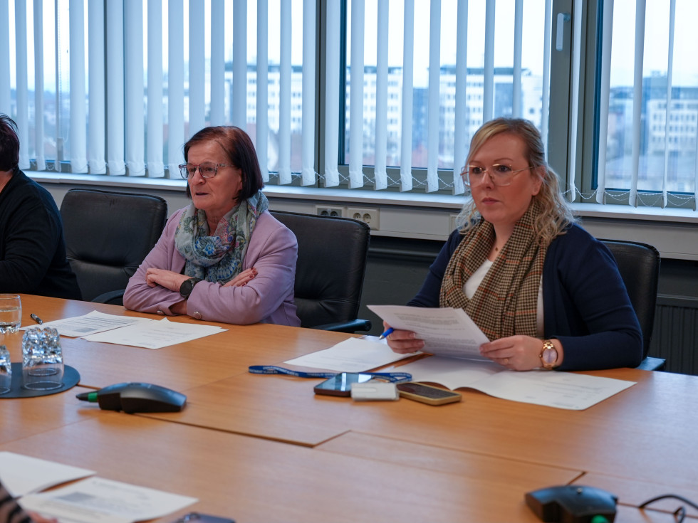 Več žensk sedi za dolgo leseno mizo in se pogovarja. 