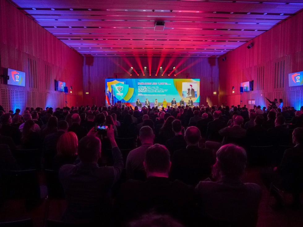 Pogled na polno dvorano. V ospredju je oder na katerem sedijo govorci