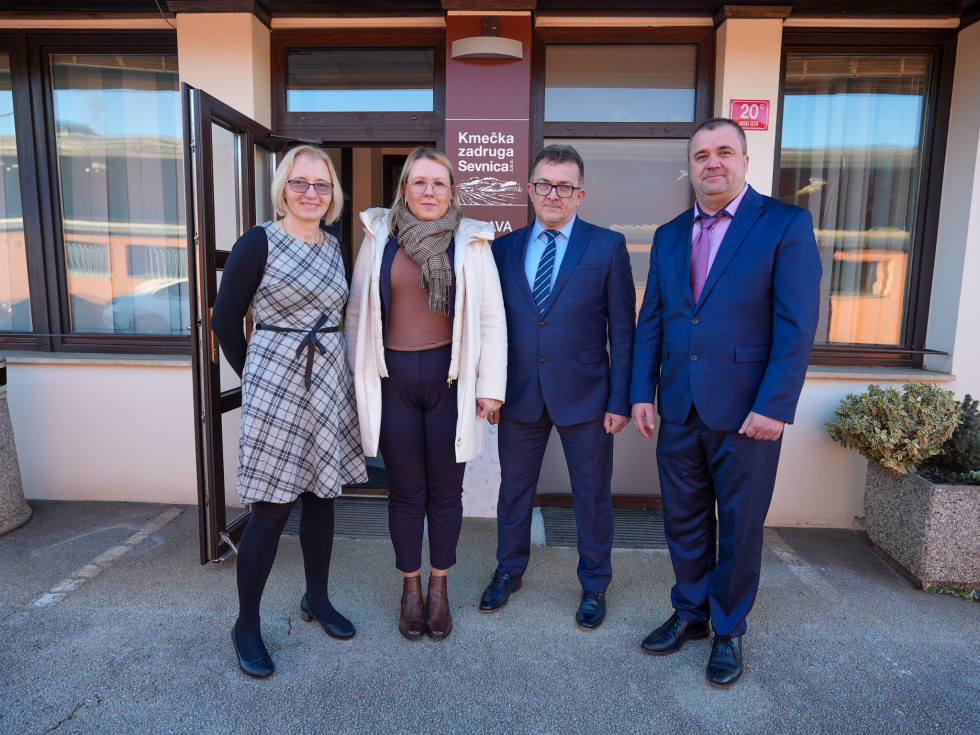 Štiri osebe stojijo pred stavbo. Pri vhodu napis: Kmečka zadruga Sevnica.