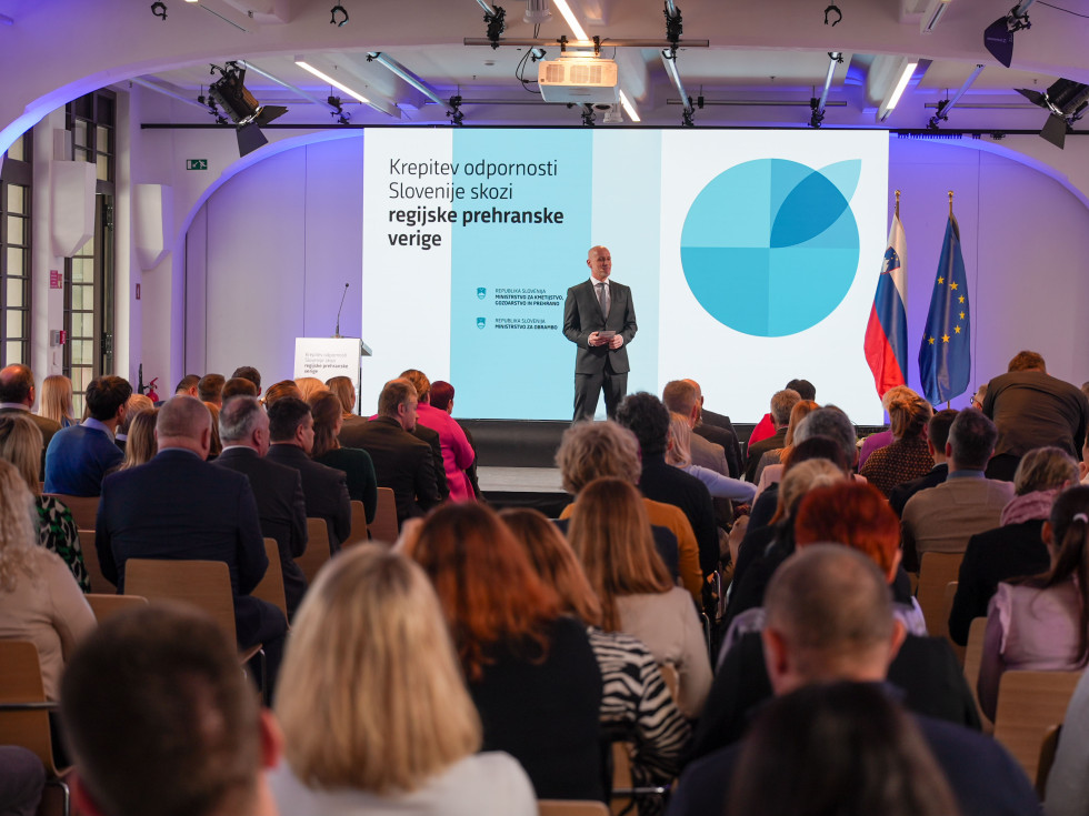 dvorana polna ljudi, ki sedijo, na odru voditelj