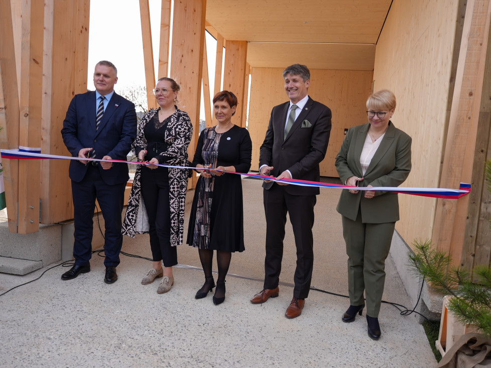 Več oseb stoji pred veliko leseno stavbo in reže trak. 