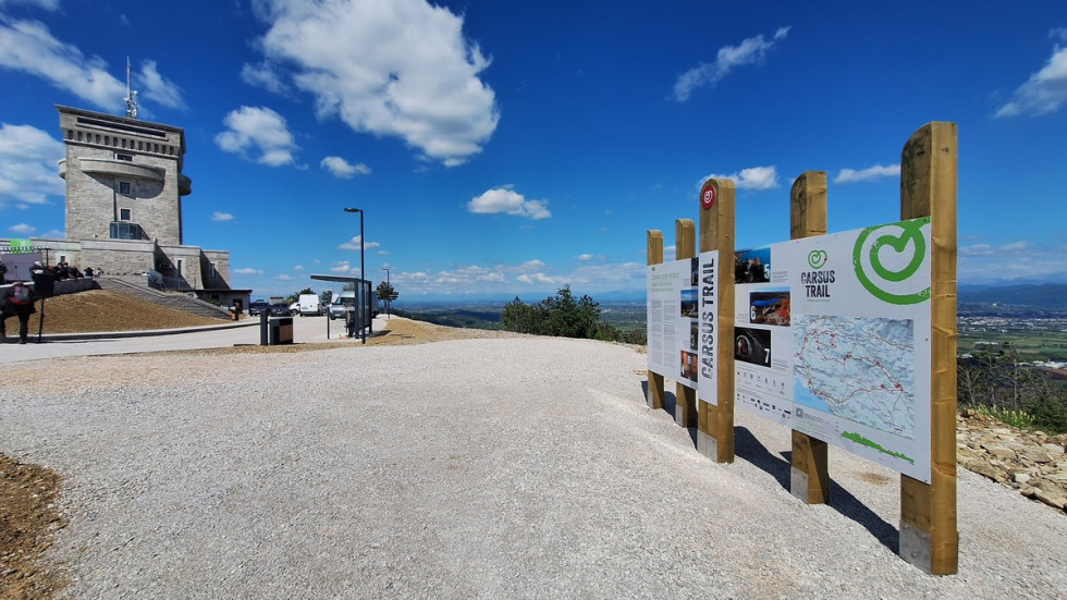 Pogled na veliko parkirišče ob njem so razstavne table. 