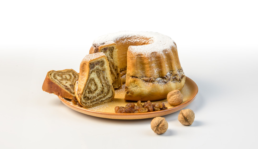 Pogled na razrezano potico. Postavljena je na leseno desno, ob njej so pa rozine. Posuka je s sladkorjem. 