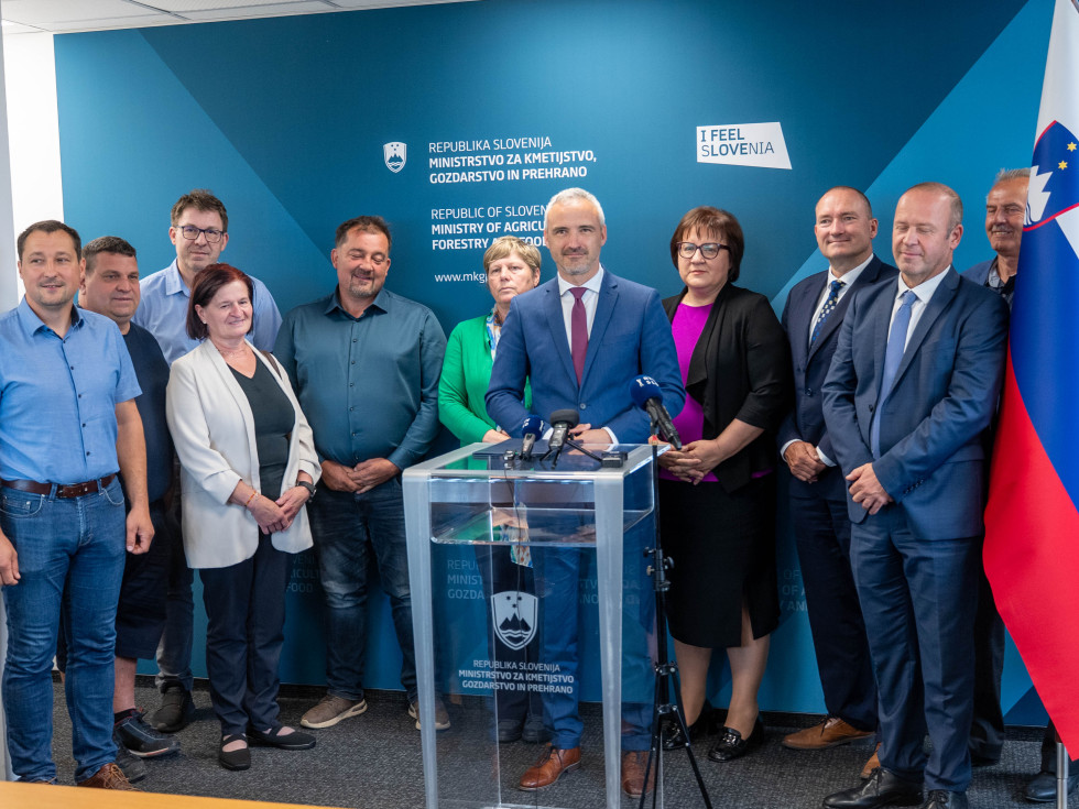 Skupina predstavnikov različnih institucij stoji ob govorniškem pultu na uradnem dogodku.