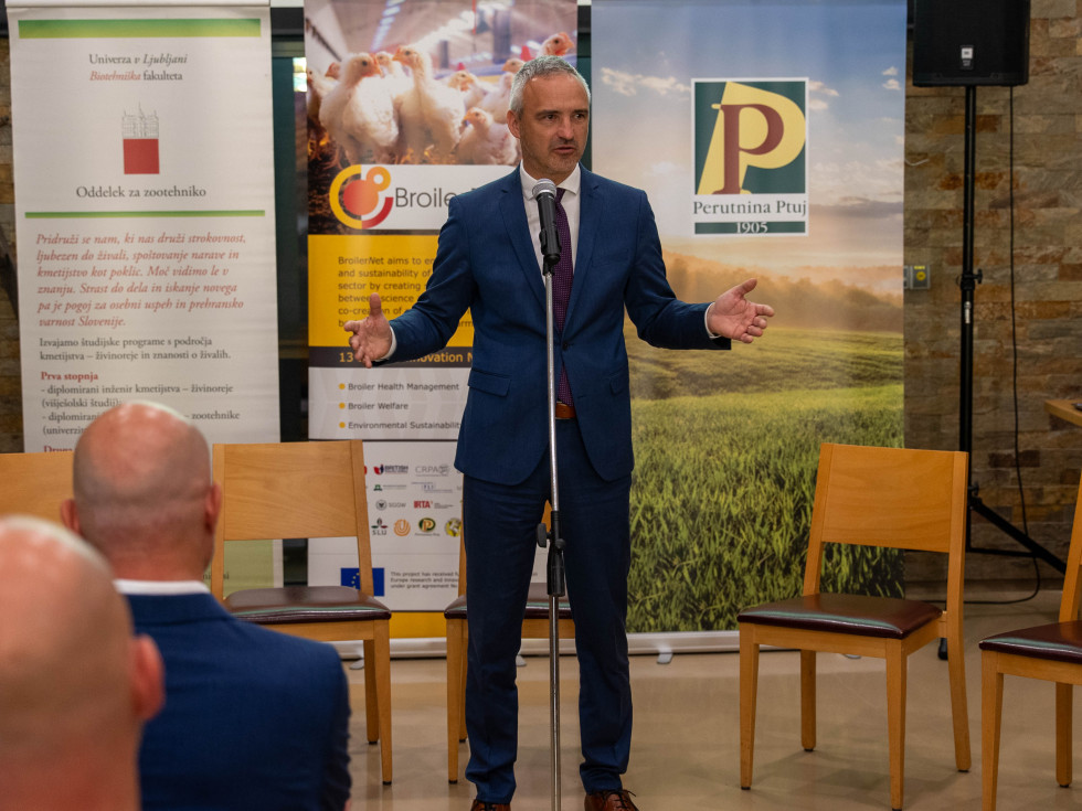 Minbibster stoji na govorniškem odru z odprtimi rokami nasmeja pred mikrofonom