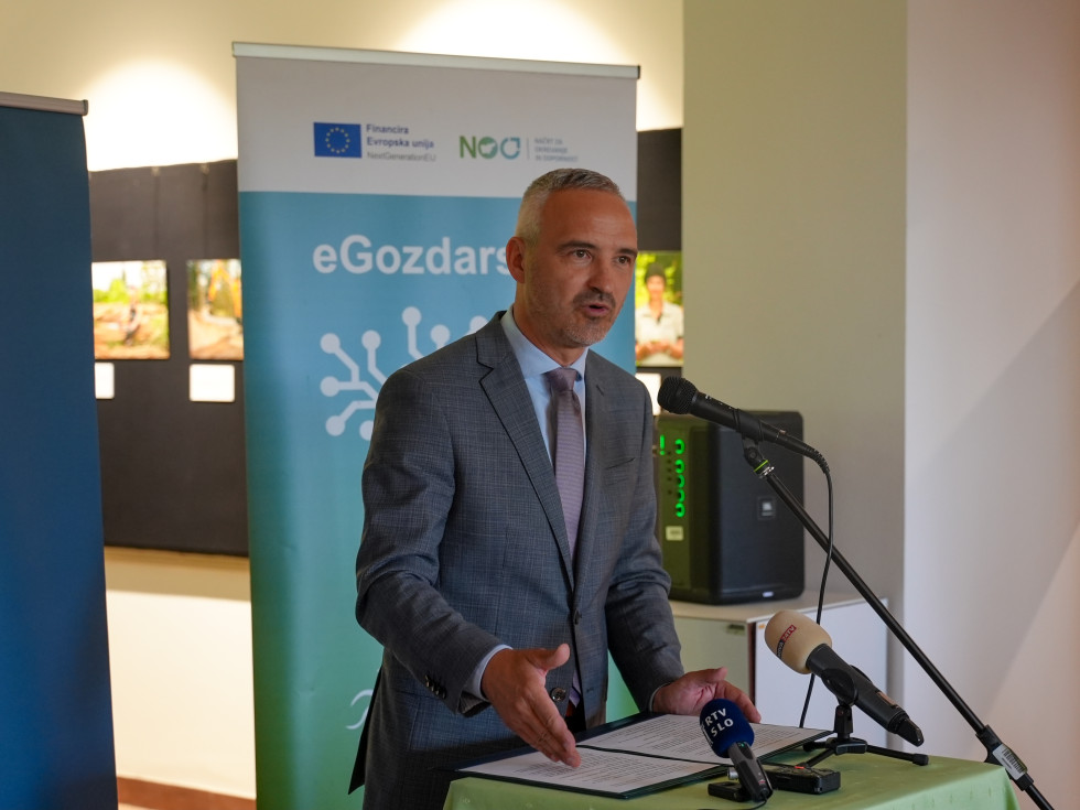 Minister stoji v avli za govorniškim pultom med pozdravnim govorom