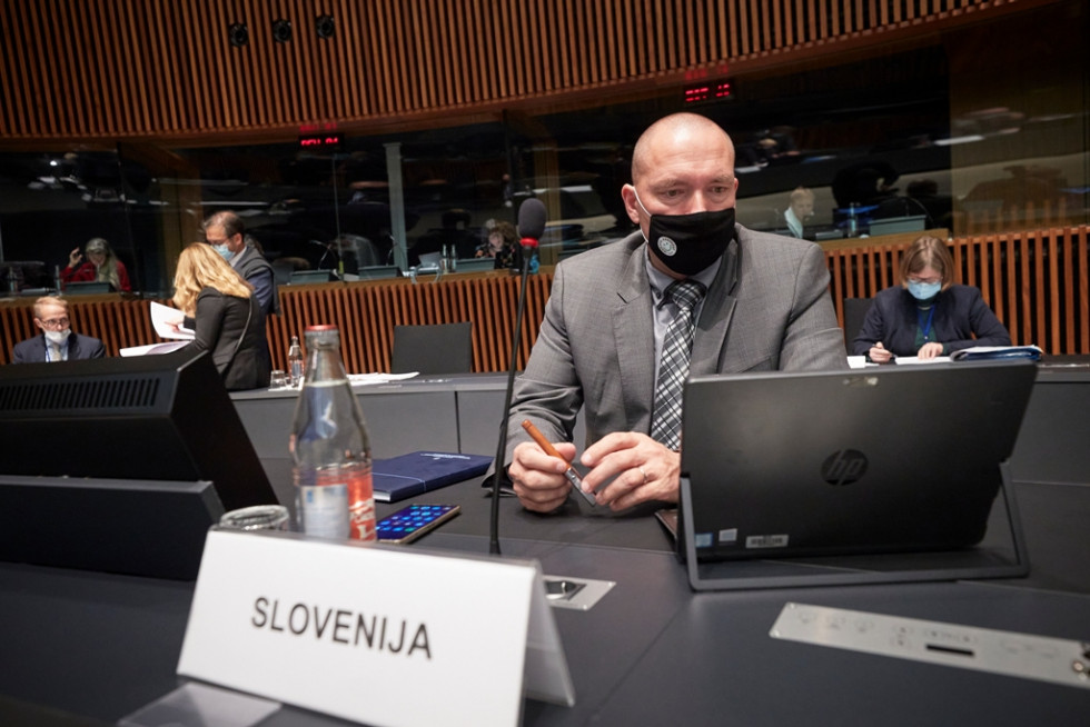 Minister v sivi obleki in z masko sedi za mizo v razpravni dvorani