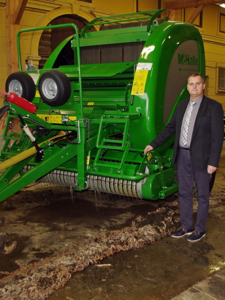 Oseba stoji ob novo kupljeni kmetijski mehanizaciji. 