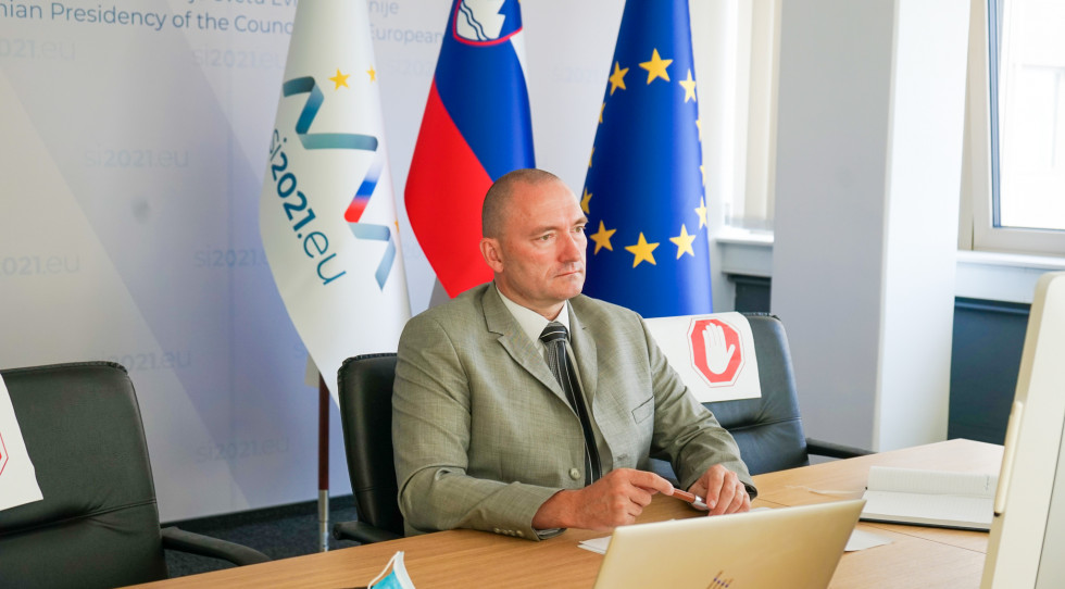 Minister v sivi obleki med sestankom sedi za mizo in spremlja dogajanje na računalniku 