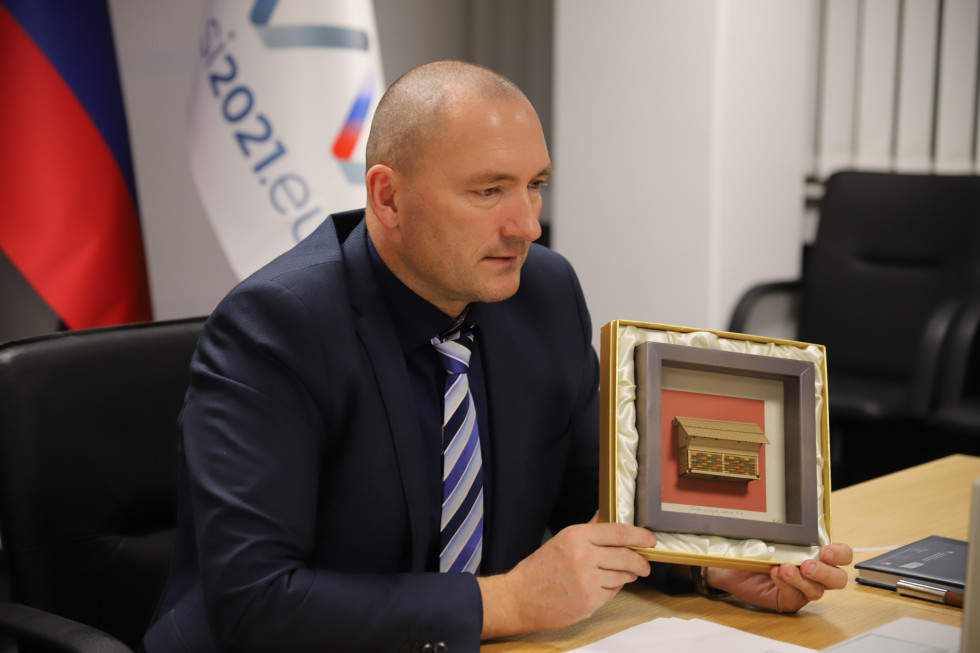 Minister gleda v ekran. V rokah ima repliko čebelnjaka. 