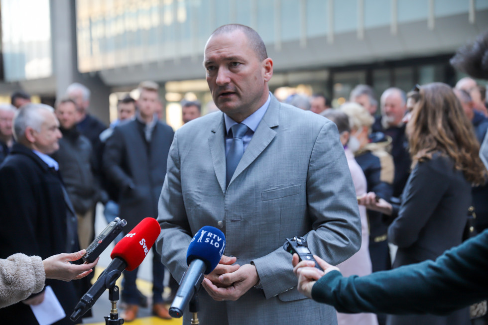 Minister stoji pred televizijskimi mikrofoni. V ozadju stojijo predstavniki kmetov in ga poslušajo. 