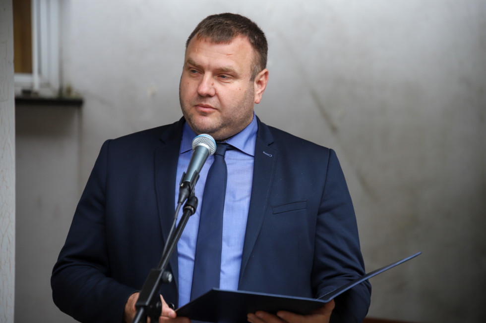 Državni sekretar stoji pred mikrofonom in govori. 