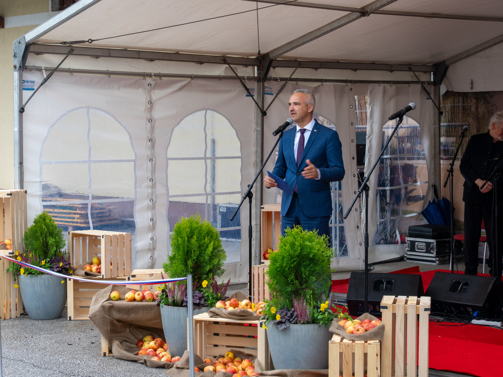 Minister stoji za govorniškim pultom in govori. 