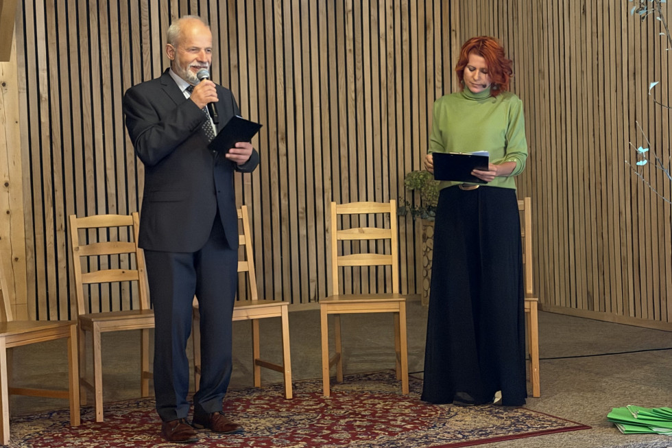 Državni sekretar stoji na odru in govori. V rokah drži mikrofon. 