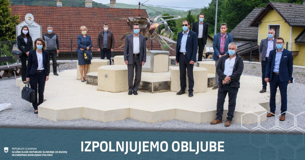 Ljudje z zaščitnimi maskami stojijo ob spomeniku čebele.