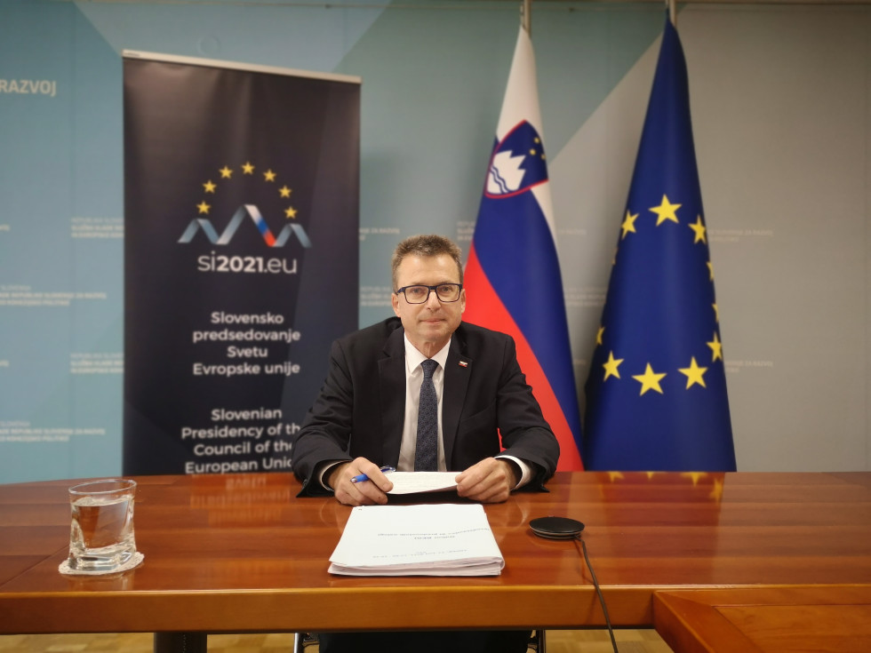Minister Černač sedi za mizo. V ozadju slovenske zastave in napis slovenskega predsedstva Svetu EU