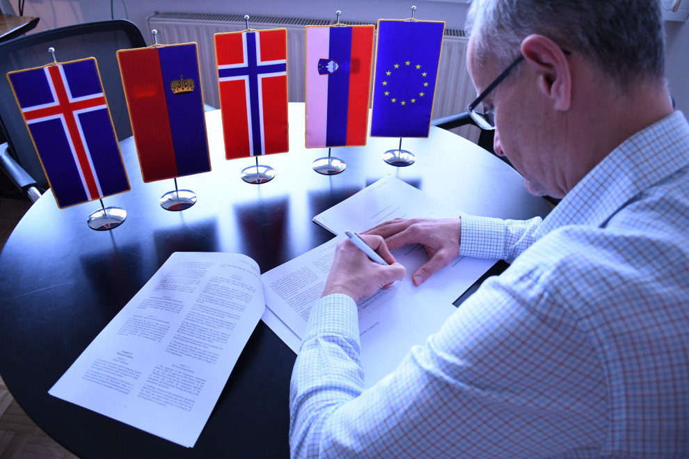 Moški podpisuje dokument. Na mizi so namizne zastavice EU, Slovenije, Norveške, Lihtenštajna in Islandije.