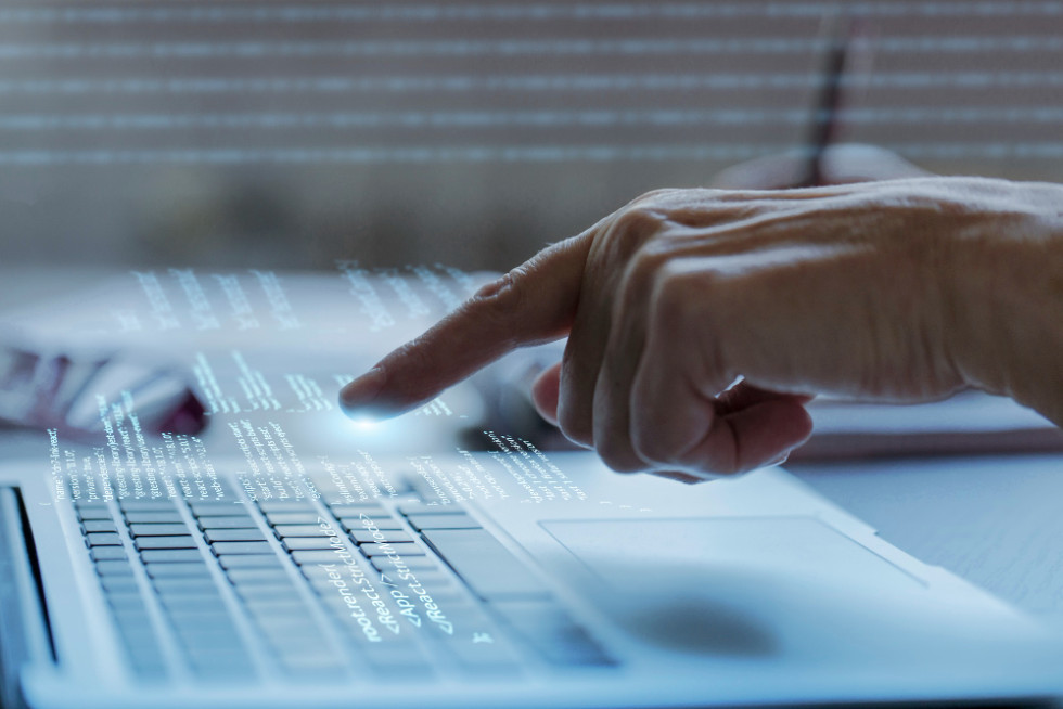 An open laptop on the table, a woman's hand with an outstretched index finger approaching it. 