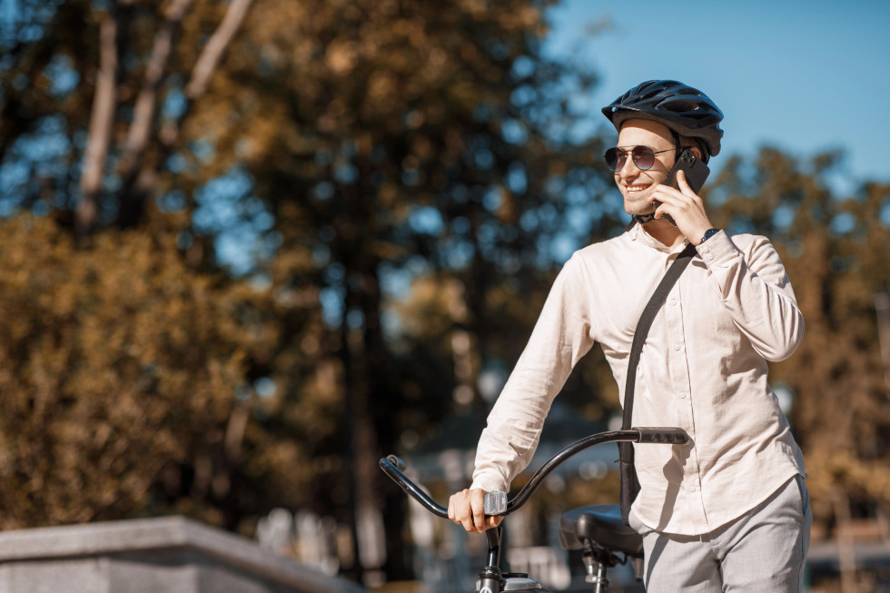 Oseba hodi ob kolesu s telefonom v roki in čelado na glavi.