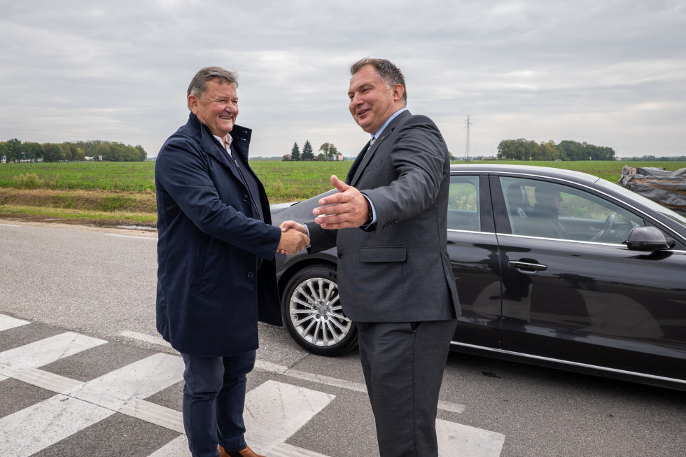 Dva moška se rokujeta, v ozadju avto