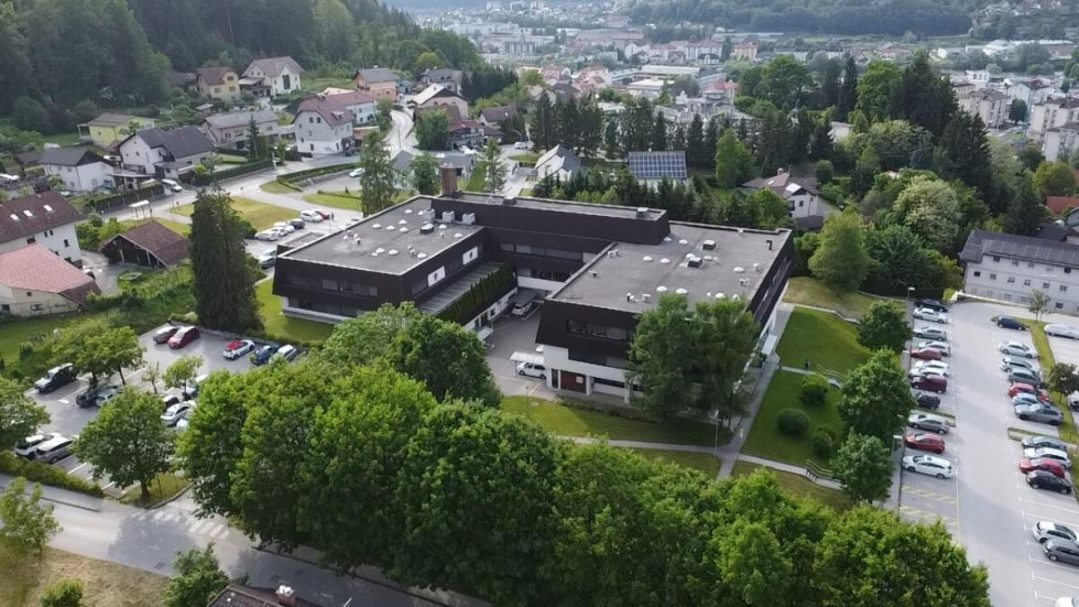 Zračni posnetek stavbe Zdravstvenega doma Litija, v ospredju drevesa, v ozadju mesto Litija.