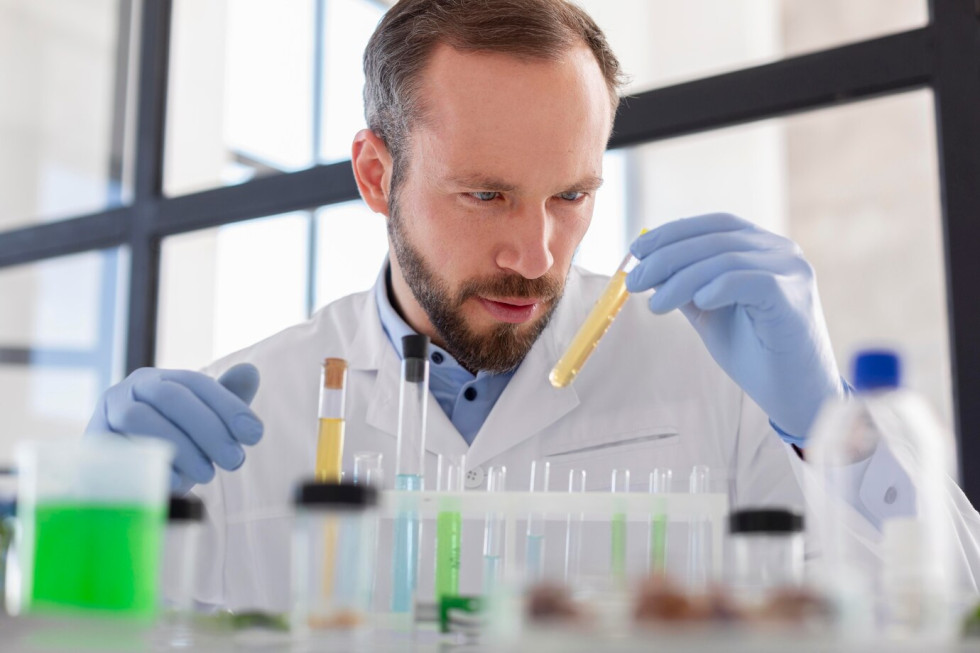 Simbolična fotografija znanstvenika v laboratoriju, ki rokuje z epruvetami.