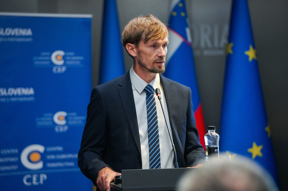 Srečko Đurov, stoji za govornico in govori. Zadaj zastave.