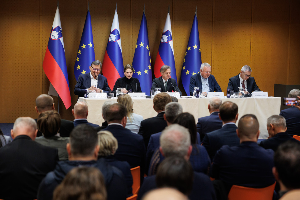 Srečanje županov in gospodarstvenikov z Vlado. Člani vlade sedijo za omizjem v dvorani. 