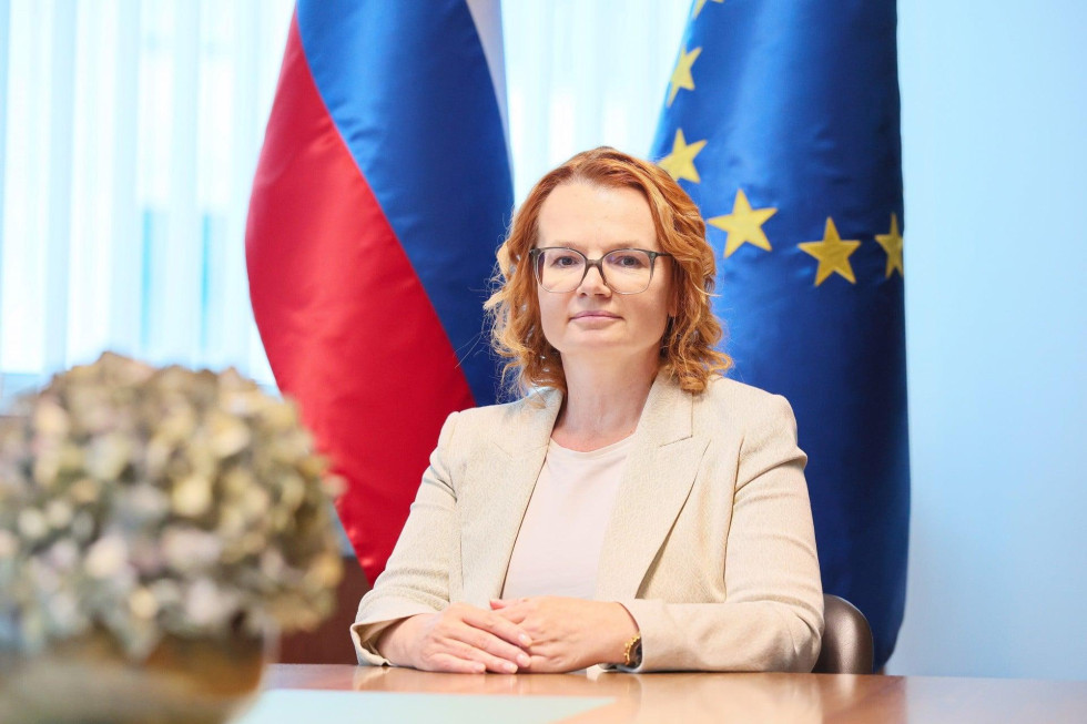 Ministrica dr. Monika Kirbiš Rojs sedi za mizo. Za njo sta postavljeni slovenska in evropska zastava.