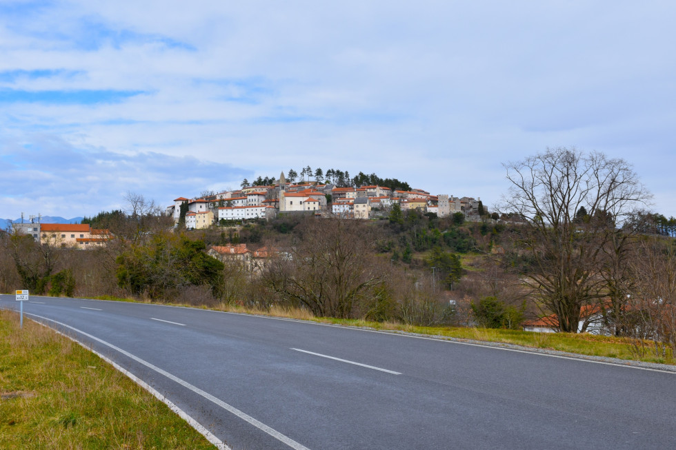 Pogled na kraško cestno infratrukturo. V ozadju naselje na hribu.