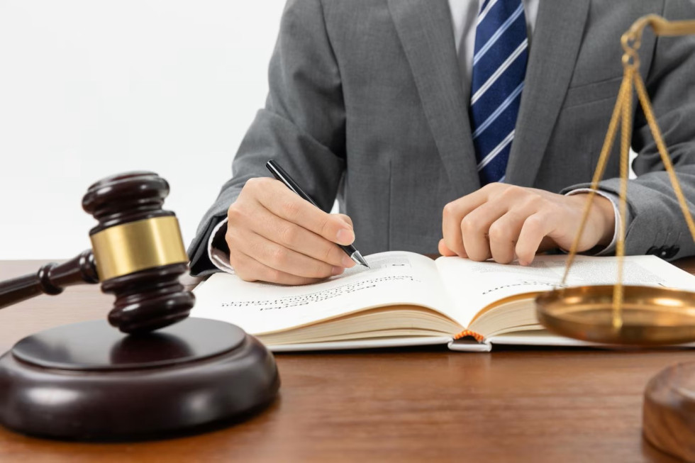 Symbolic photograph showing a man's hand in business clothes writing in a notebook. A judge's gavel is on the table in front of the judge..