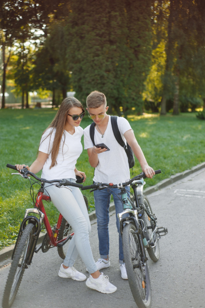A man and a woman on a bike in the park, looking at their phones.