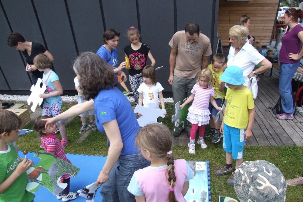 Otroci skupaj s straši pred Slovenskim planinskim muzejem v Mojstrani  sestavljajo mozaik z motivom gora
