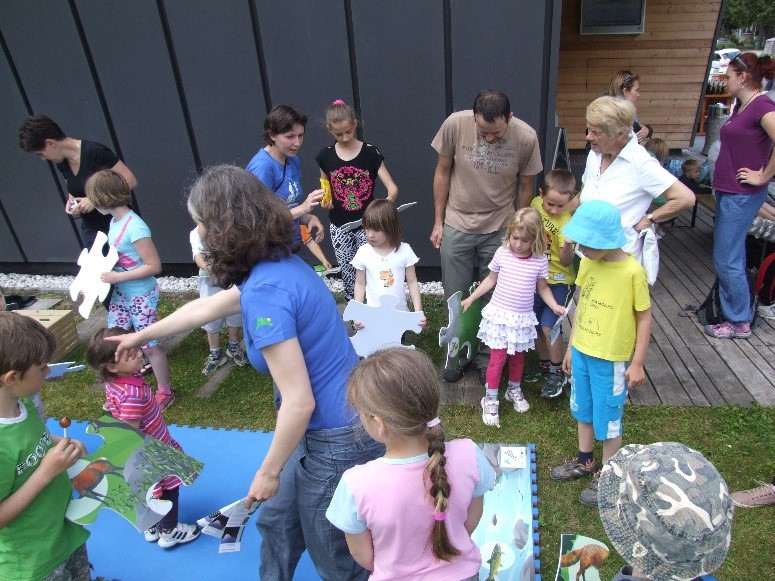 Otroci skupaj s straši pred Slovenskim planinskim muzejem v Mojstrani  sestavljajo mozaik z motivom gora