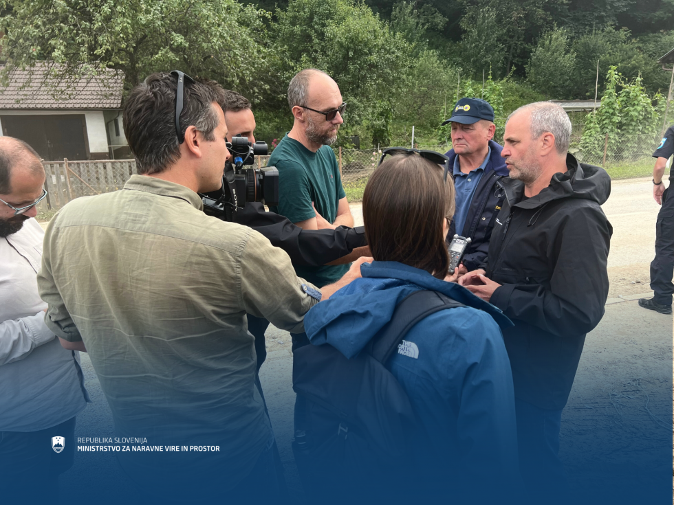 Minister Brežan podaja izjavo na terenu, ob njem novinarji in snemalec