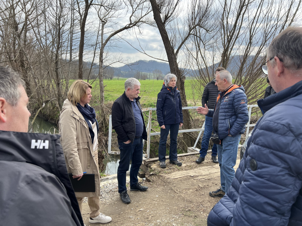 predstavniki ministrstva, direkcije in kmetov stojijo na brežini reke