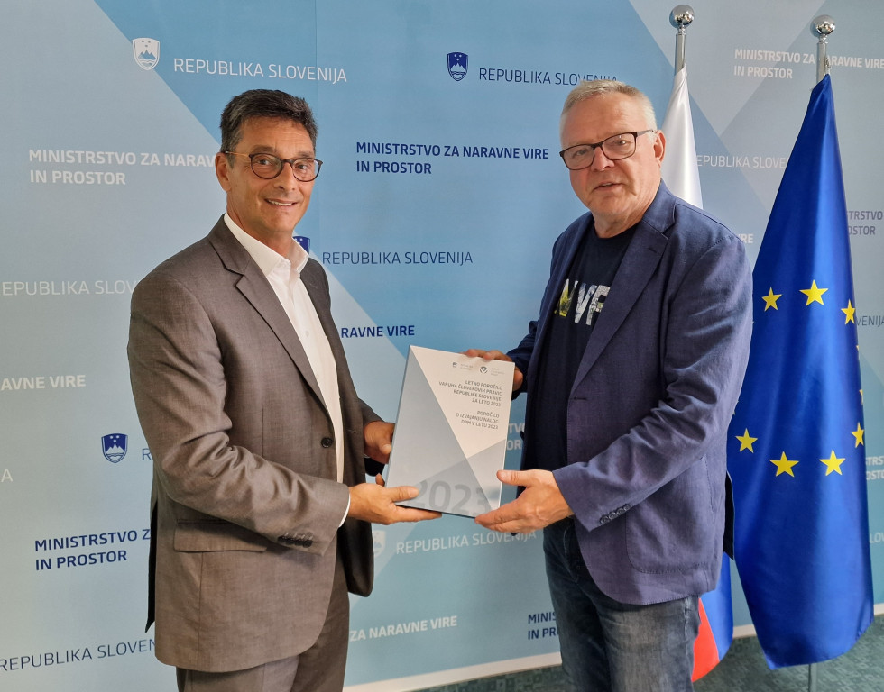 Novak in Svetina med predajo poročila, v ozadju slovenska in evropska zastava