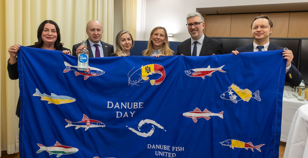 Udeleženci slovesnosti stojijo ta transparentom Mednarodne komisije za varstvo reke Donave