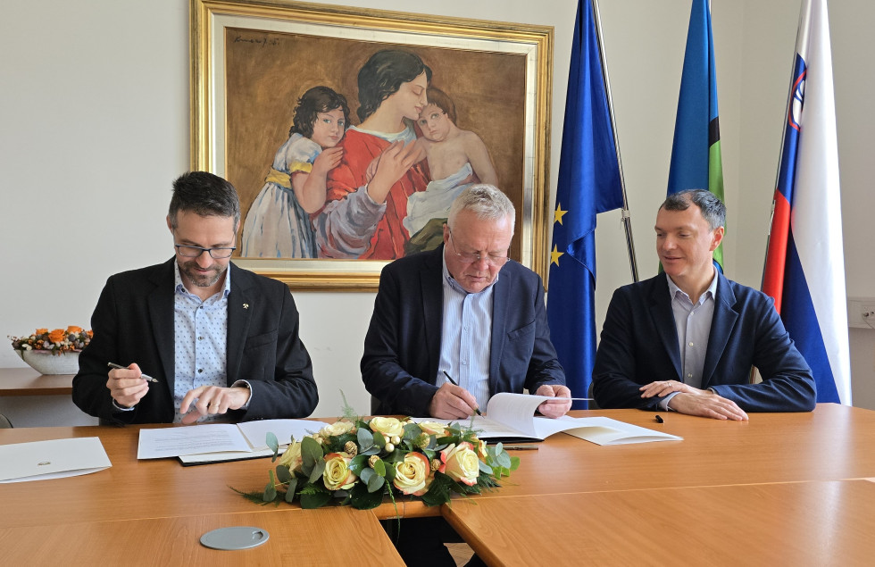 Minister Novak in direktor premogovnika Velenje Rošer stojita ob predaji podpisanega aneksa, v ozadju slika in zastave